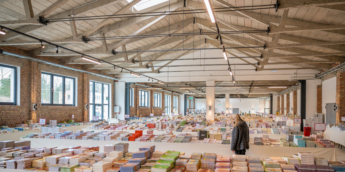 Ein Mann geht im Bücherzirkus Prora zwischen den Tischen voller Bücher umher und schaut sich um.